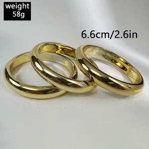 Detail of three chunky minimalist gold bangles with a high-polished mirror finish.