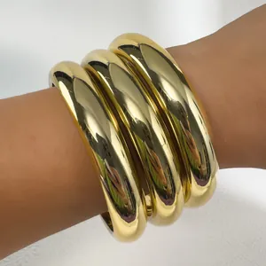 Macro detail of three chunky polished gold bangles featuring a glossy metallic finish