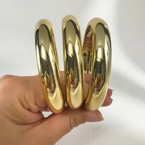 Detailed close-up view of three chunky polished gold bangles being held in hand