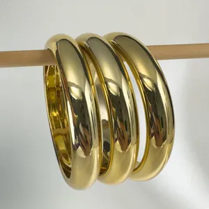 Detailed view of three minimalist polished gold chunky bangles hanging on a wooden rod