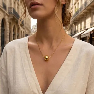Detail view of a polished gold ball pendant on a delicate chain worn by a model