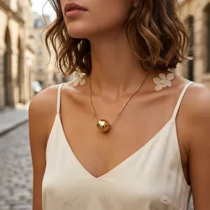 Close-up of a minimalist gold plated ball pendant necklace on a female model