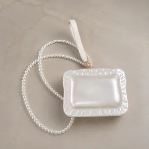 Close-up of elegant pearlescent acrylic clutch bag with pearl chain and wrist strap.
