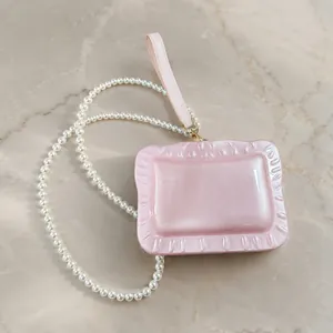 Detail showing the pink pearlescent acrylic texture and pearl strap of the evening bag.