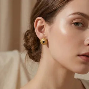Close-up of vintage round gold stud earrings featuring an embossed pattern and black stone center