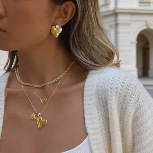 Detail von 18K vergoldeten Ohrringen und Halsketten mit Hammerschlag-Herz auf Modell.