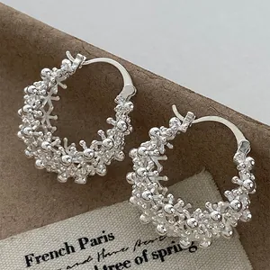 Macro view of silver hollow round basket hoop earrings with intricate textured bubble design.