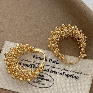 Detail shot of golden hollow flower basket hoop earrings with textured bead design