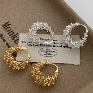Close-up of gold and silver textured hollow basket hoop earrings on a vintage label