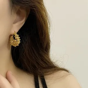 Detailed close-up view of elegant gold hollow floral basket hoop earring worn by model