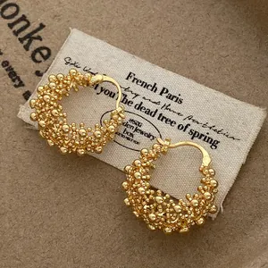 Close-up of gold-colored textured flower basket hoop earrings resting on white canvas.
