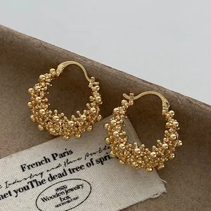 Detail of golden hollow hoop earrings with intricate beaded flower basket design.