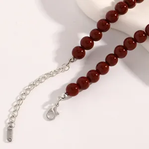 Makrodetail einer dunkelroten Perlenkette mit Edelstahl-Karabinerverschluss und Kette.
