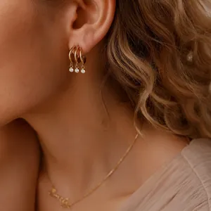 Detailed shot of gold stainless steel hoop earrings with small round zircon charms.
