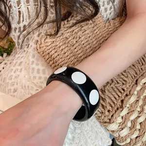 Détail d'un bracelet jonc en résine à pois noirs et blancs au style rétro Y2k