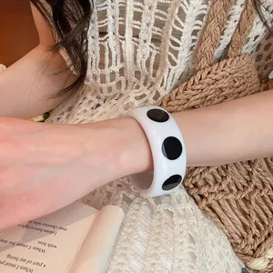 Gros plan d'un bracelet jonc en résine blanche à pois noirs sur le poignet d'une femme