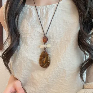 Close-up of vintage amber resin teardrop pendant necklace on model's cream top.