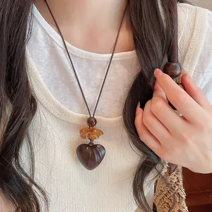 Close-up of vintage resin heart pendant necklace worn over a white knit top for women.
