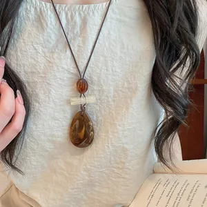 Detail showing the texture of a vintage resin teardrop pendant necklace on a model
