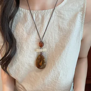 Close-up of vintage amber-toned resin teardrop pendant on long sweater chain for women