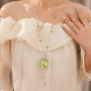 Detailansicht einer Perlenkette mit grünem Erdbeeranhänger und Perlen an einem Modell.