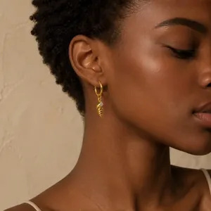 Detailansicht eines goldenen Muschel-Ohrrings mit Strasssteinen an einem Model.