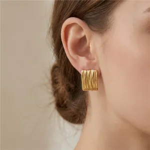 Gros plan de boucles d'oreilles en acier inoxydable doré 18K à rayures gaufrées sur l'oreille.
