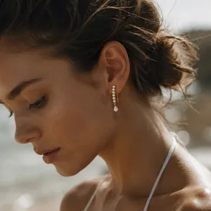 Close-up detail of elegant gold-toned titanium steel earrings with sparkling zircons on model