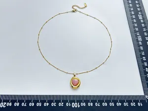 Stainless steel gold necklace with pink heart crystal pendant next to a measuring ruler