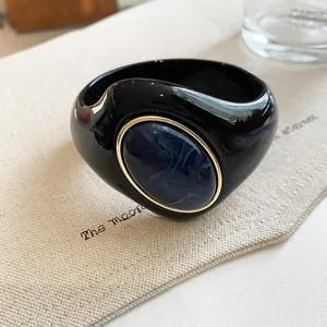 Detailed close-up of a bold black acrylic bangle with a marbled blue oval inlay