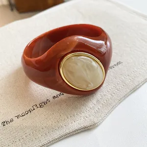 Close-up of marbled terracotta acrylic bangle with cream oval inset and gold trim