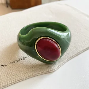 Macro detail of a chunky marbled green acrylic bangle with an oval red resin inlay