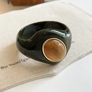 Exaggerated dark green acrylic bangle featuring a marbled amber stone in a gold rim
