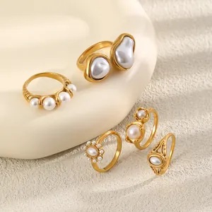 Détail de cinq bagues en acier doré 18K avec divers motifs de perles d'imitation.