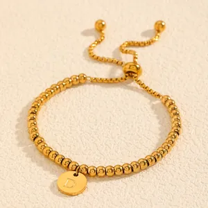 Gros plan d'un bracelet ajustable en acier titane doré avec une breloque disque lettre D