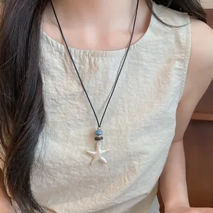 Detail view showing a minimalist silver starfish pendant on a stylish black cord necklace.