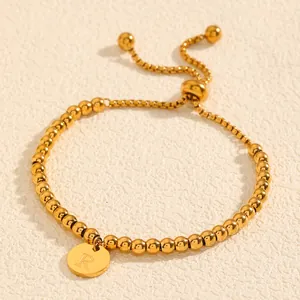 Détail en gros plan d'un bracelet en perles d'acier titane doré avec breloque lettre R