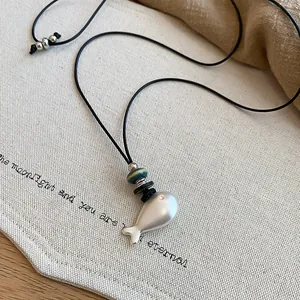Detailed macro view of matte silver fish pendant necklace with black cord and rustic beads