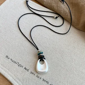 Macro view of minimalist silver teardrop pendant necklace with black cord and beads