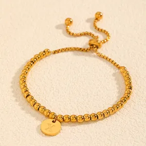Gros plan détaillé d'un bracelet en perles d'acier doré avec pendentif gravé de la lettre X