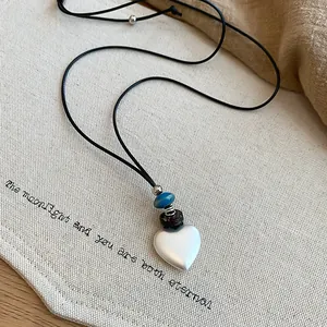 Close-up of a matte silver heart pendant on a black cord over textured canvas background.