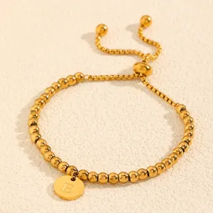 Bracelet élégant en acier titane doré avec un pendentif circulaire à initiale 'E'.