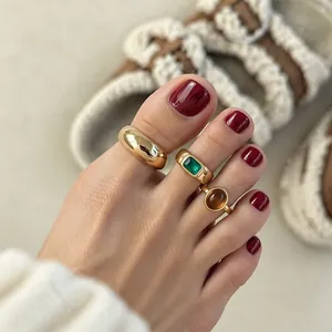 Dettaglio macro di eleganti anelli per piedi in oro con gemme verdi e marroni su un piede.