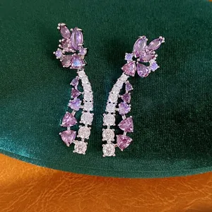 Luxuriöse violette und weiße Kristall-Blumenohrringe auf grünem Samthintergrund präsentiert