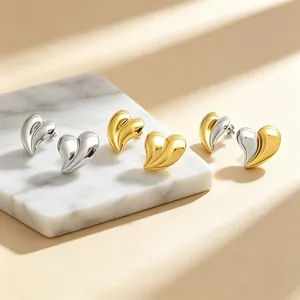 Gros plan de boucles d'oreilles coeur 3D en acier plaqué or 18K, versions or et argent.