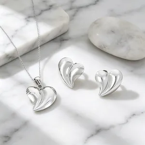 Vue détaillée d'un ensemble collier et boucles d'oreilles cœur 3D argenté sur marbre.