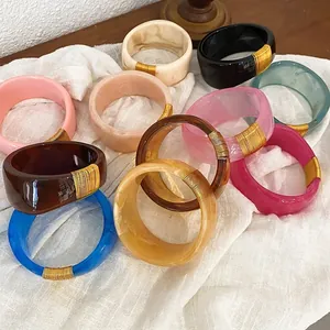 Assorted wide marbled resin bangles with elegant gold wire wrap on white linen fabric.