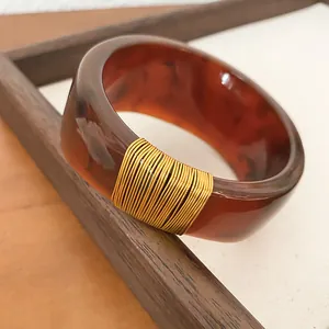 Macro view of the wide tortoise shell resin bangle featuring elegant gold wire wrap detail