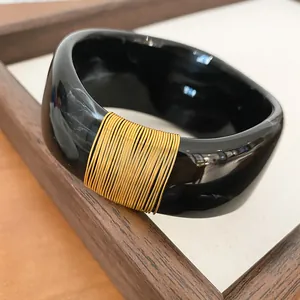 Macro view of marbled black resin bangle with elegant gold wire wrap detail texture