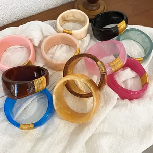 Detail view of various colorful wide resin bangles featuring elegant gold wire wrap accents
